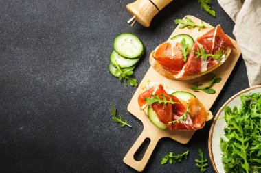 Aperatif crostini, krem peynirli sandviç, prosciutto, salatalık ve roka. Kopyalama alanı olan üst görünüm.