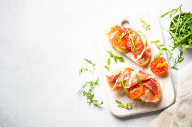 Açık sandviç, krem peynirli aperatifler, beyaz masada prosciutto ve roka. Kopyalama alanı olan üst görünüm.