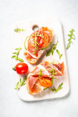 Açık sandviçler, jambonlu aperatifler ve beyaz arka planda kesilmiş roka. Üst görünüm.