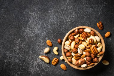 Koyu taş masadaki ahşap kasede fındık çeşitleri. Kaju, fındık, badem, Brezilya fındığı ve ceviz. Kopyalama alanı olan üst görünüm.