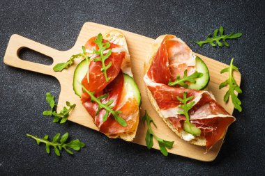 Sandviçleri krem peynirli, jambonlu, salatalıklı ve roka dilimli açın..