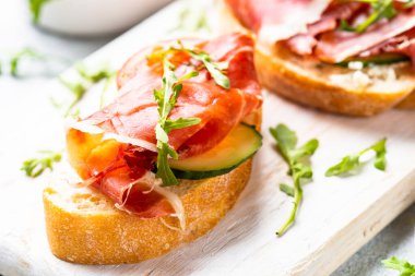 Beyaz arka planda kesme tahtasının üzerinde prosciutto ve roka ile sandviç açın. Üst görünüm.