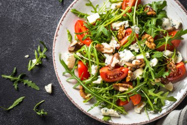 Arugula salad with tomatoes, blue cheese and walnuts. Healthy vegetarian dish. Top view image, close up.