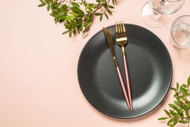 Table setting with black plate, glasses, cutlery and flowers at pink background. Creative table decoration. Top view image with copy space.