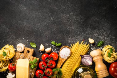 Siyah arka planda makarna malzemeleri. Çiğ makarna, parmesan, taze domates ve fesleğen. Kopyalama alanı olan üst görünüm.