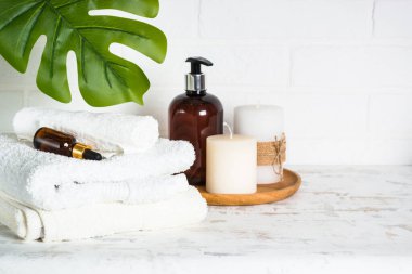 Banyodaki spa ürünleri. Beyaz banyoda bir şişe sabun, kozmetik ve beyaz havlular..
