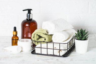 Banyodaki spa ürünleri. Beyaz banyoda bir şişe sabun, kozmetik ve beyaz havlular..