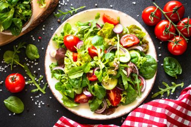 Siyah masada beyaz tabakta salata yaprakları ve sebzeler. İçerikli üst görünüm.