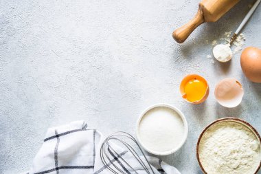 Arkaplan malzemeleri pişiriyorum. Un, şeker, yumurta ve diğer şeyler hafif taş masada. Kopyalama alanı olan üst görünüm.