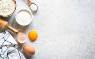 Flour, sugar, eggs and rolling pin at light stone table. Top view with copy space.