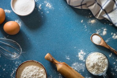 Arkaplan malzemeleri pişiriyorum. Yemek çerçevesi. Un, şeker, yumurta ve merdane mavi taş masada. Kopyalama alanı olan üst görünüm.