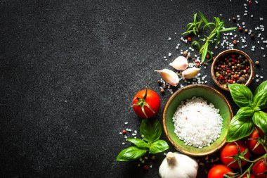 Taze sebzeler, şifalı otlar ve baharatlarla siyah taş masada yemek. Fotokopi alanı ile pişirme malzemeleri.