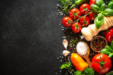 Taze sebzeler, şifalı otlar ve baharatlarla siyah taş masada yemek. Fotokopi alanı ile pişirme malzemeleri.