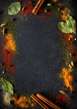Spices and herbs on black slate background. Pepper, turmelic, dill, cinnamon, basil, rosemary, chilly, cardamom. Top view with copy space, vertical image.