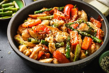 Chicken stir fry with vegetables and sesame in the skillet. Close up.