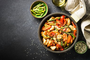 Chicken stir fry with vegetables in the skillet at black stone background. Top view with copy space.