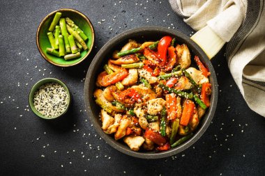 Chicken stir fry with vegetables in the skillet at black stone background. Top view with copy space.