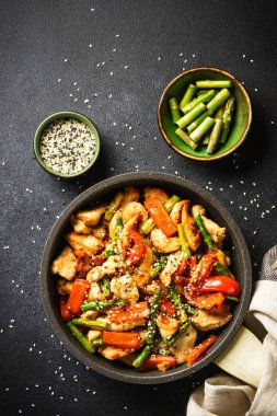 Chicken stir fry with vegetables in the skillet at black stone background. Top view with copy space.