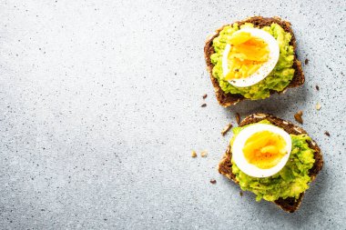 Avocado sandwich. Whole grain bread with avocado and boiled eggs at stone table.