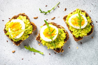 Open sandwich. Whole grain bread with avocado and boiled eggs. Top view on stone background.