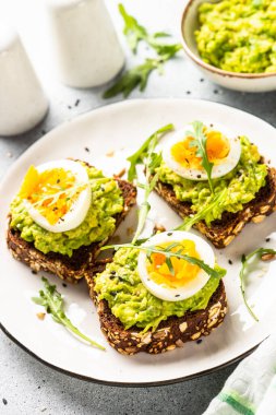 Open sandwich. Whole grain bread with avocado and boiled eggs. Top view on white kitchen table.