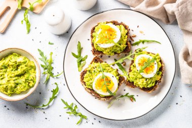 Open sandwich. Whole grain bread with avocado and boiled eggs. Top view on white kitchen table.