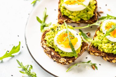 Avocado sandwich. Whole grain bread with avocado and boiled eggs at white plate. Close up image.