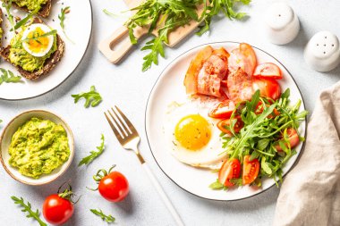 Healthy breakfast or lunch. Becon, eggs, toast with avocado and fresh salad. Top view on white.