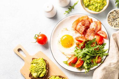 Becon, eggs, toast with avocado and fresh salad. Healthy food, paleo diet. Top view on white kitchen table.