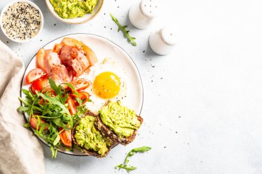 Becon, eggs, toast with avocado and fresh salad. Healthy food, paleo diet. Top view on white kitchen table.
