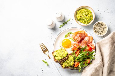 Becon, eggs, toast with avocado and fresh salad. Healthy food, paleo diet. Top view on white kitchen table.