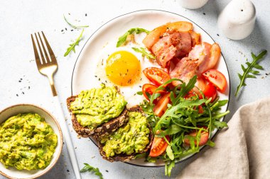 Healthy breakfast or lunch. Becon, eggs, toast with avocado and fresh salad. Top view on white kitchen table.