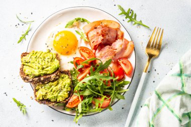 Healthy breakfast or lunch. Becon, eggs, toast with avocado and fresh salad. Top view on white kitchen table.