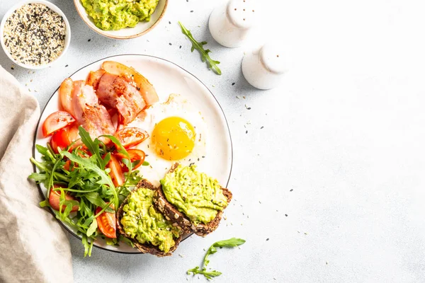 Becon, eggs, toast with avocado and fresh salad. Healthy food, paleo diet. Top view on white kitchen table.