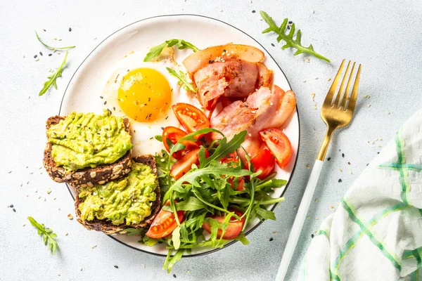 Healthy breakfast or lunch. Becon, eggs, toast with avocado and fresh salad. Top view on white kitchen table.