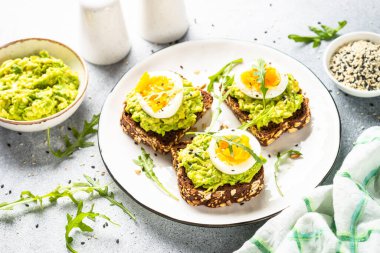 Open sandwich. Whole grain bread with avocado and boiled eggs. Top view on white kitchen table.