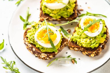 Avocado sandwich. Whole grain bread with avocado and boiled eggs with arugula. Close up image.