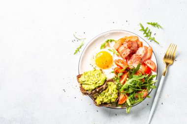 Healthy breakfast or lunch. Beacon, eggs, toast with avocado and fresh salad. Top view on white kitchen table.