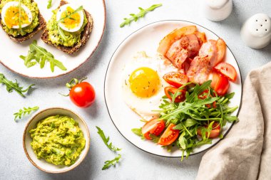 Healthy breakfast or lunch. Beacon, eggs, toast with avocado and fresh salad. Top view on white.