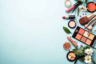 Make up professional, Cosmetic products on blue background. Cream, powder, shadow, brushes with green leaves and flowers. Top view with copy space.