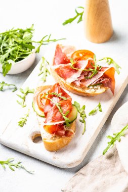 Beyaz arka planda kesme tahtasının üzerinde prosciutto ve roka ile sandviç açın. Resmi kapat.