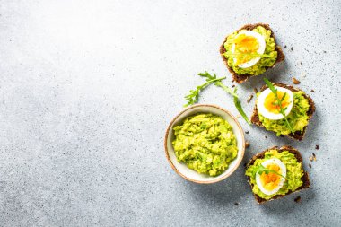 Open sandwich. Whole grain bread with avocado and boiled eggs. Top view on stone background.