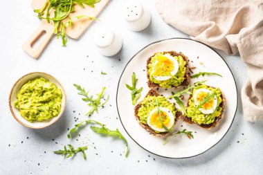 Open sandwich. Whole grain bread with avocado and boiled eggs. Top view on white kitchen table.