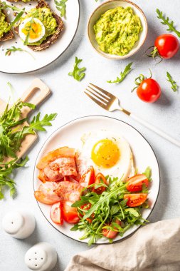 Healthy breakfast or lunch. Fried beacon, eggs, toast with avocado and green salad. Top view on white.