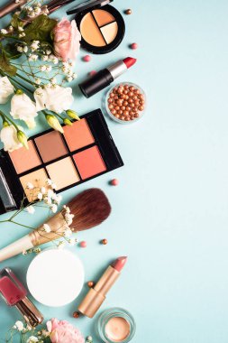 Make up professional, Cosmetic products on blue background. Cream, powder, shadow, brushes with green leaves and flowers. Top view with copy space.