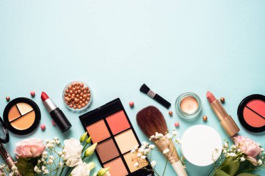 Make up professional cosmetics on blue background. Cream, powder, shadow, brushes with green leaves and flowers. Flat lay image with copy space.