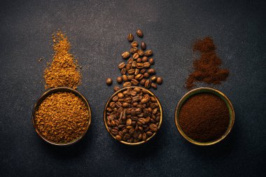 Roasted coffee beans, ground coffee and instant coffee in bowls at dark background. Top view image.