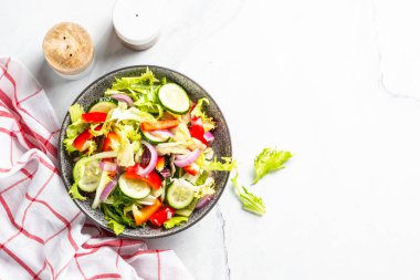 Vegan salad with green leaves, cucumber and bell pepper on white. Top view with copy space.