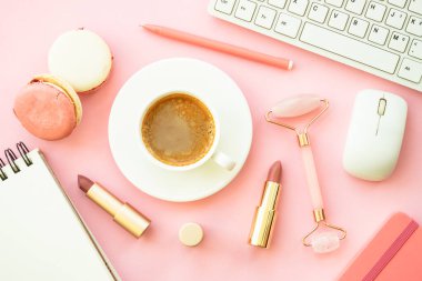Creative office workspace. Pink flat lay background with keyboard, coffee cup, macaroons and cosmetics.