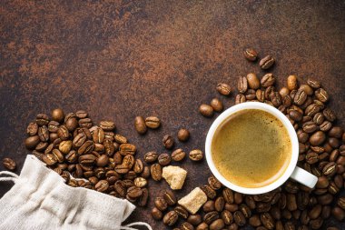 Cup of coffee and sack of coffee beans at dark table . Top view image with copy space.